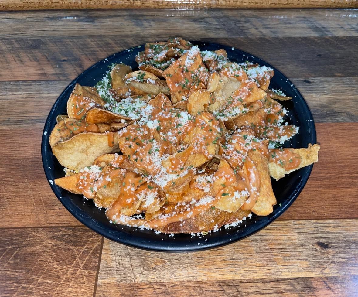 Black plate of crispy chips with orange sauce and white cheese topping.