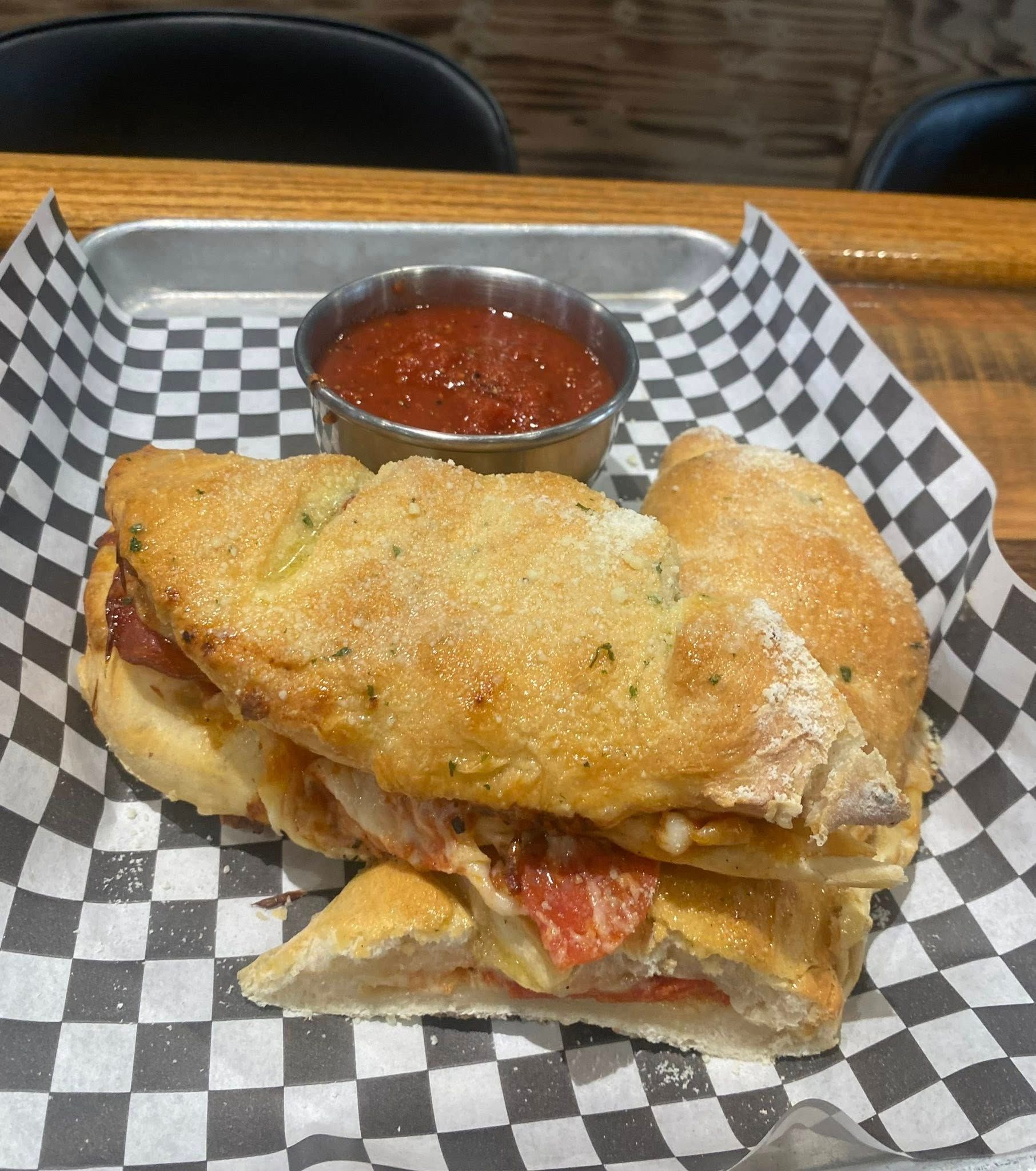 Sandwich with dipping sauce on checkered paper and a metal tray.