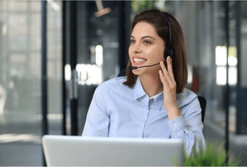 Customer support agent wearing a headset, smiling at a laptop in a modern office