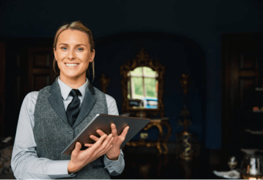 Smiling server in gray vest holding a tray in a dimly lit restaurant lounge