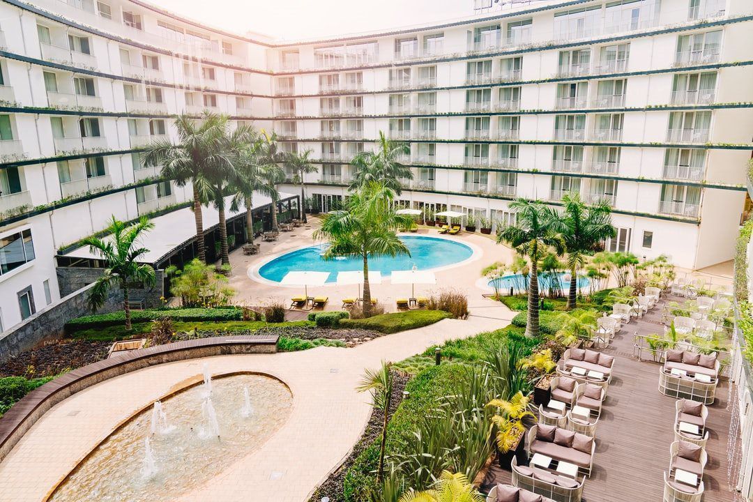 Resort courtyard with a large pool, palm trees, and lounge chairs surrounded by curved hotel balconies