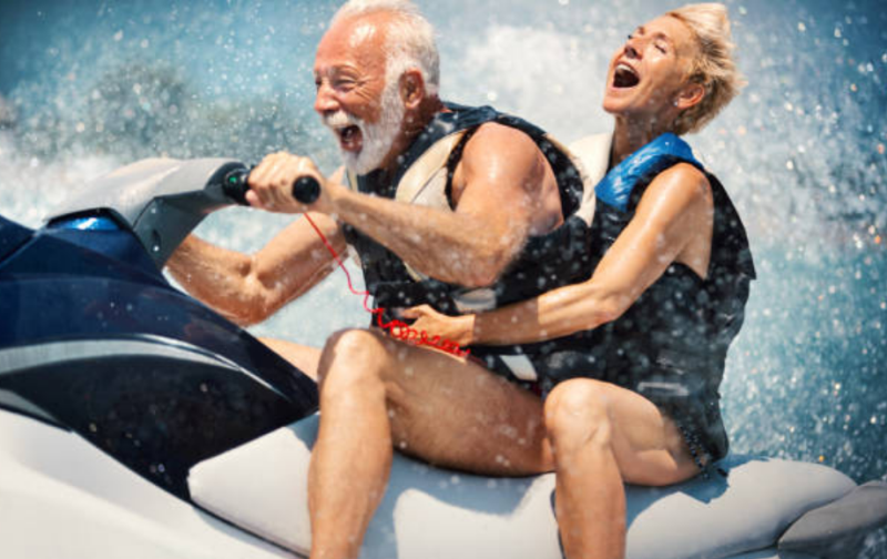 Two people riding a jet ski through splashing water, both laughing and holding on tightly