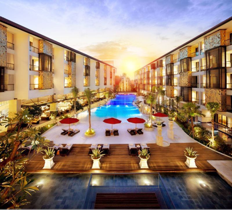 Luxury hotel courtyard with glowing pool, red umbrellas, and modern buildings at sunset