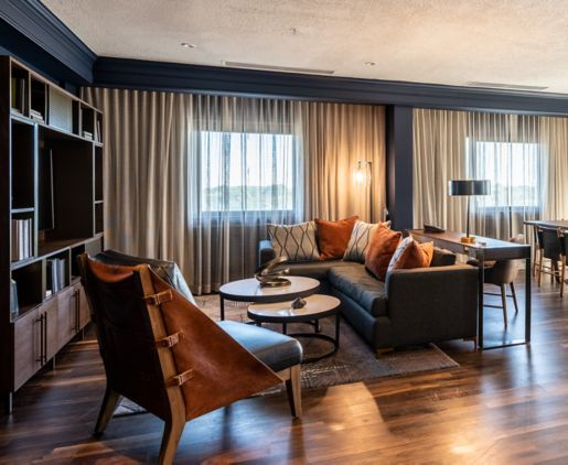 Modern living room with gray sofa, brown chairs, coffee tables, and large curtained windows