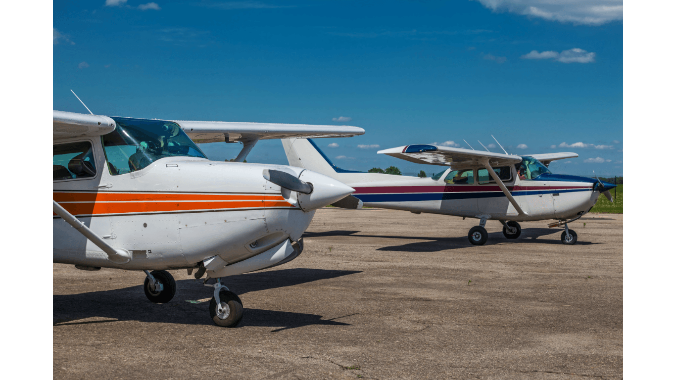 Two small airplanes parked on a tarmac under a bright blue sky.