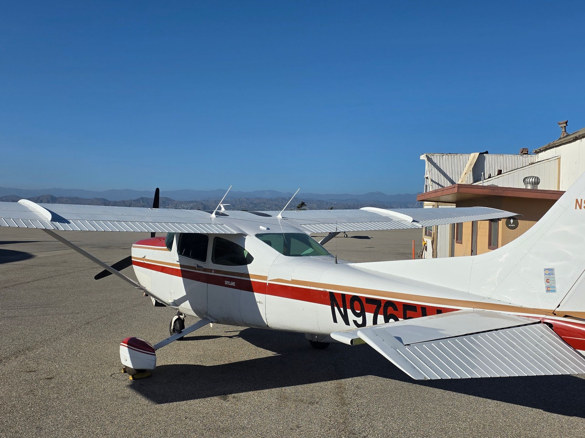 White and red Cessna airplane parked on the tarmac with a blue sky in the background.