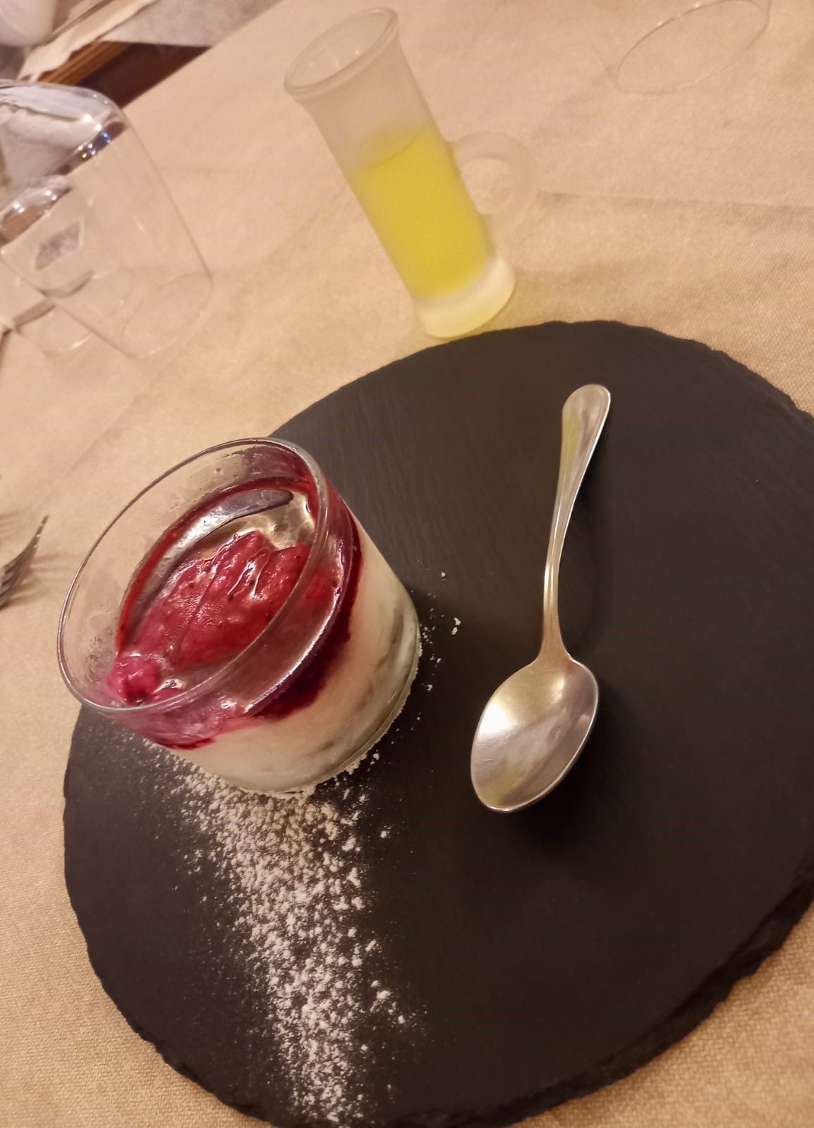 Un dessert con un cucchiaio e un bicchierino sullo sfondo
