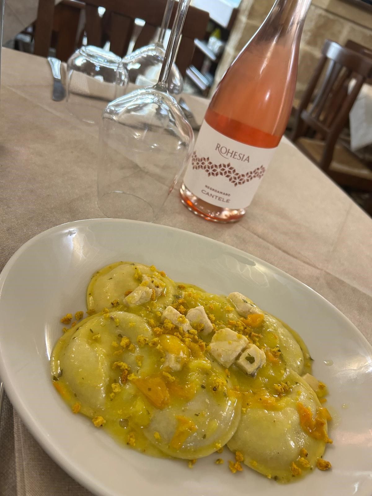 Un piatto di ravioli accanto a una bottiglia di vino su un tavolo.
