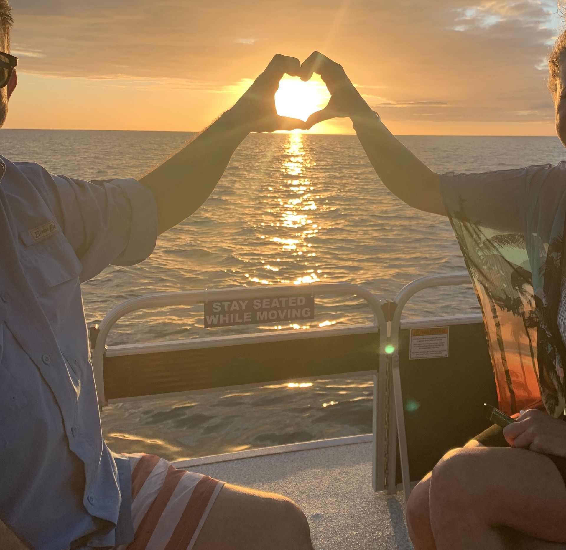 Two people making a heart shape with their hands at sunset over the ocean