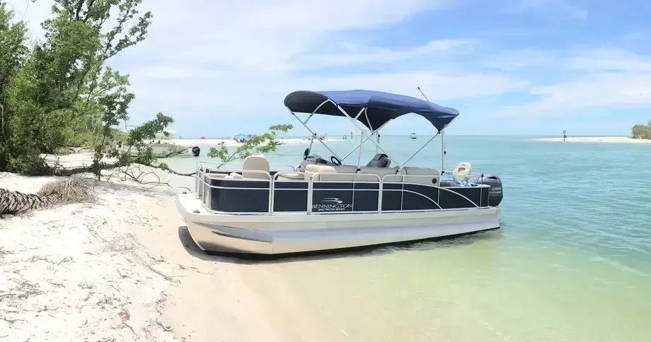 Pontoon boat with blue canopy parked on a sandy tropical beach beside clear water
