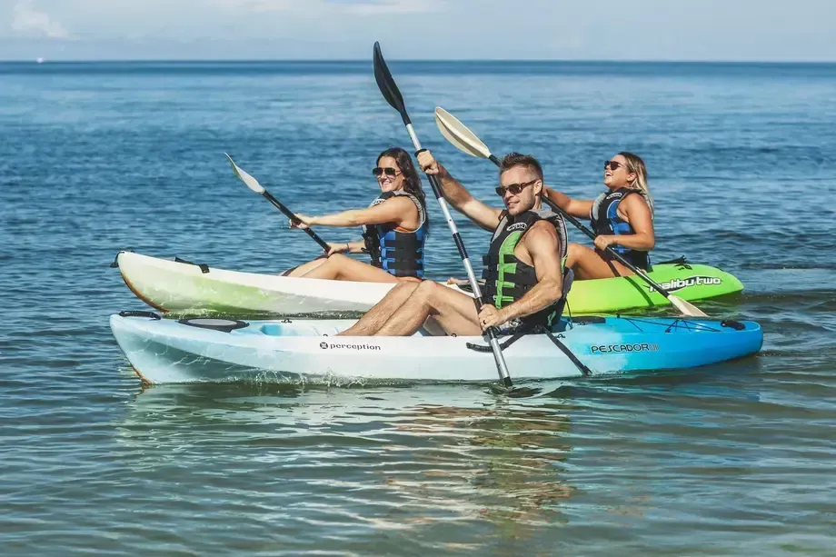 Three people kayaking on calm blue water under a clear sky