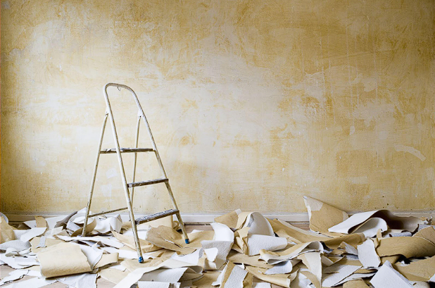 A ladder is sitting in a room with a pile of wallpaper on the floor.