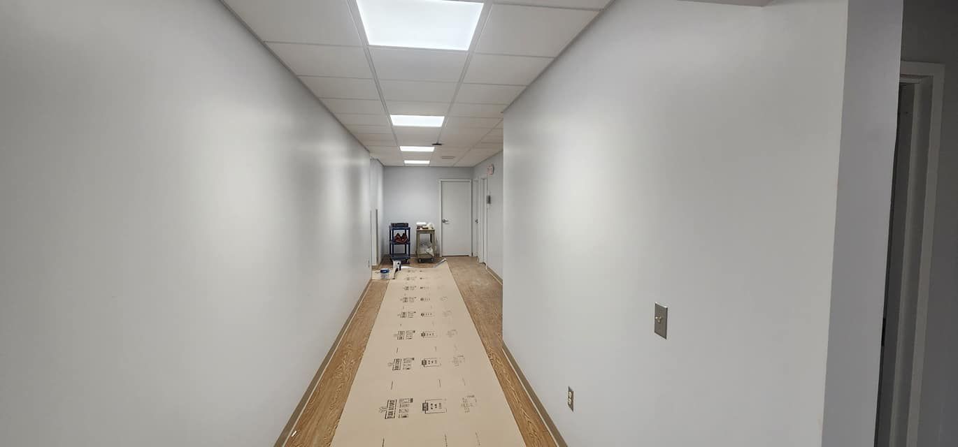 A long hallway with white walls and wooden floors is being painted.