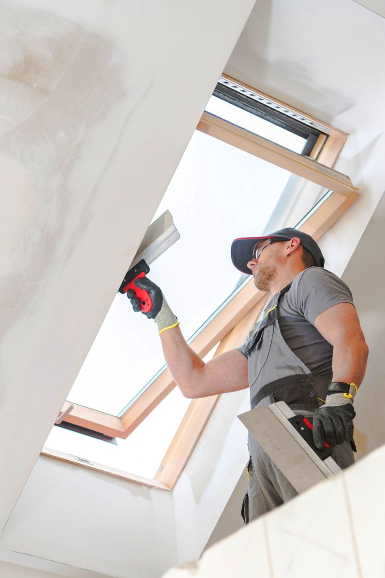 A man is plastering a ceiling in a room with a skylight.