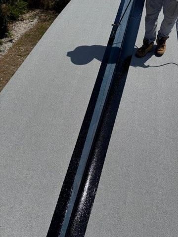 Person standing on a rooftop beside a long black seam in gray roofing material