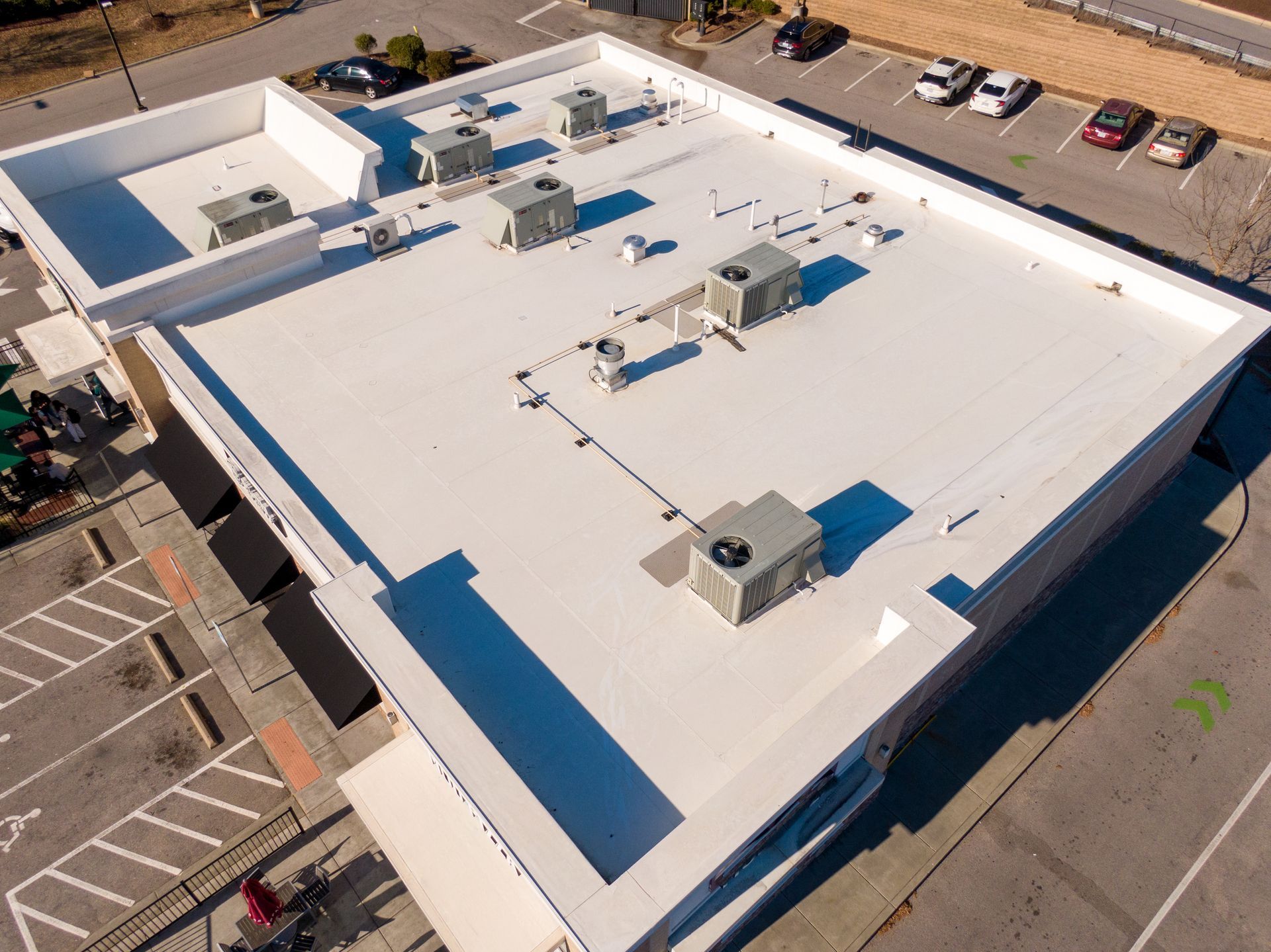Aerial view of a white flat-roofed commercial building with HVAC units and surrounding parking lot.
