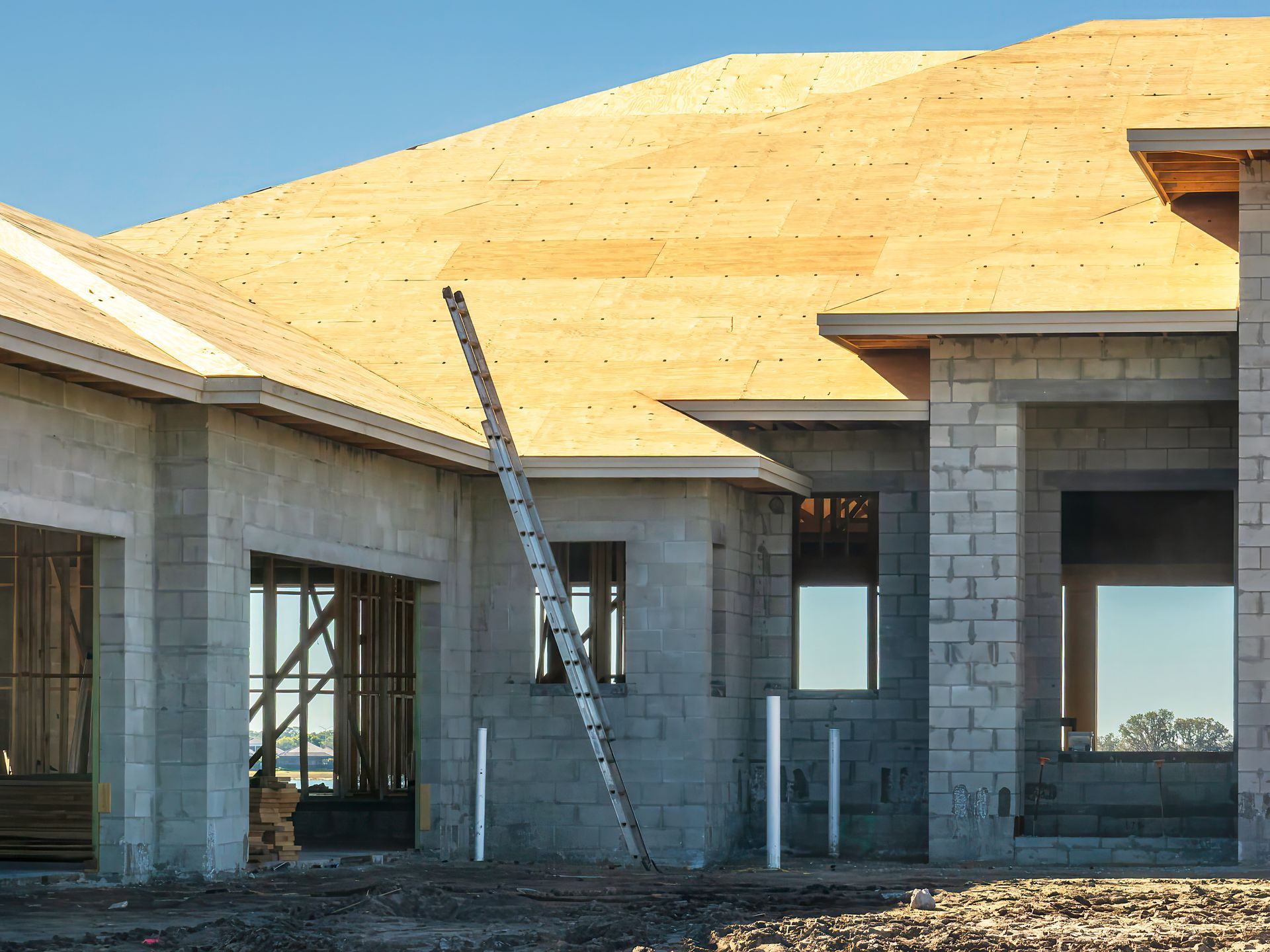 Partially built cinder block house with a wooden roof frame and ladder under construction