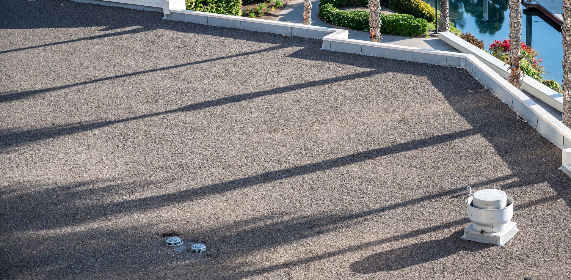 Rooftop gravel area with a small white vent and a metal railing casting shadows in sunlight