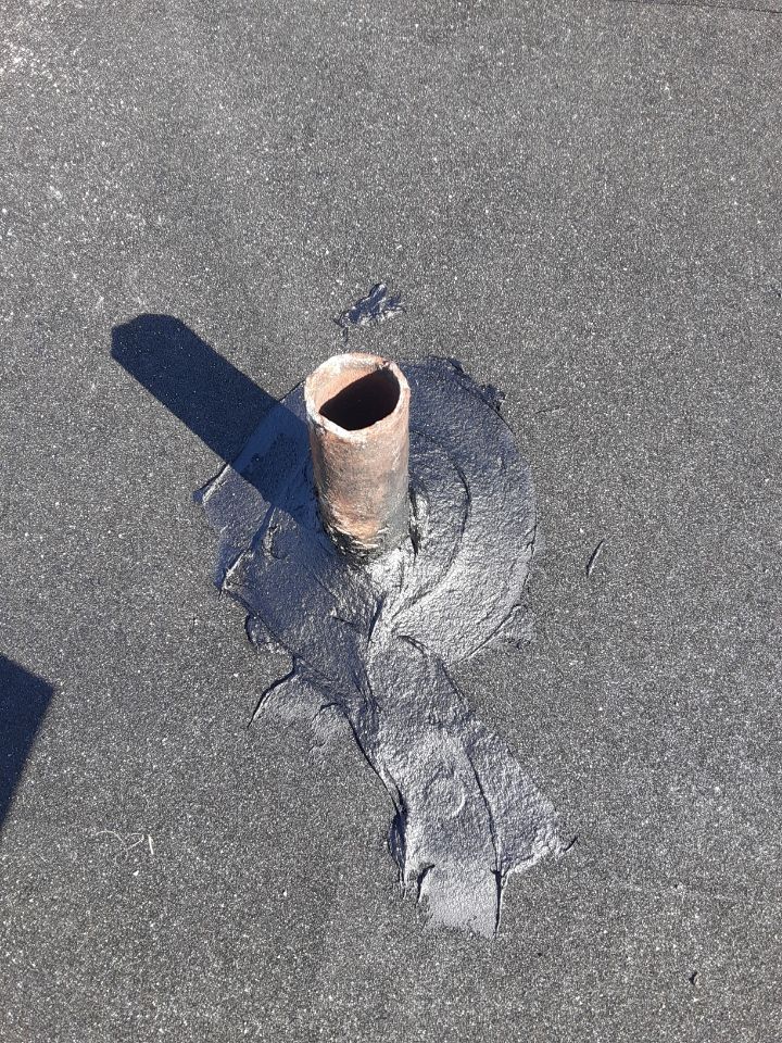 Damaged roof vent pipe with cracked sealant on gray roofing material