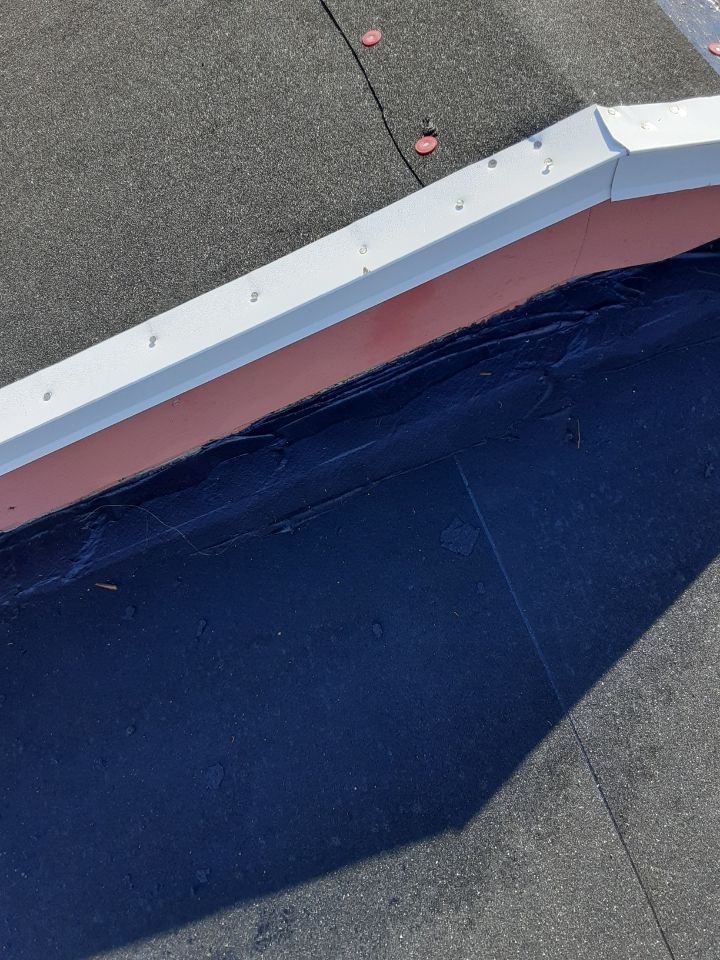 Rooftop edge with white trim and pink flashing beside dark blue roofing under sunlight
