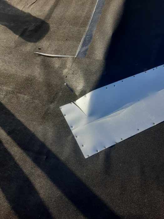 Close-up of a white metal flashing panel on a dark shingled roof with tape seam and nail heads