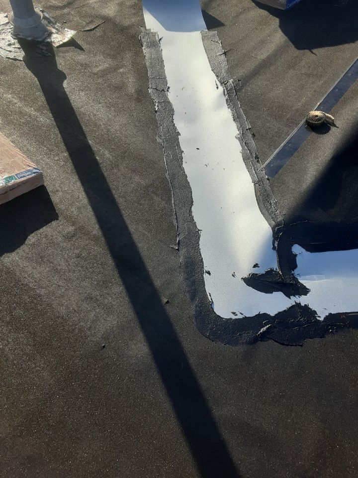 Close-up of a roof seam with fresh white sealant over dark roofing material and shadows.