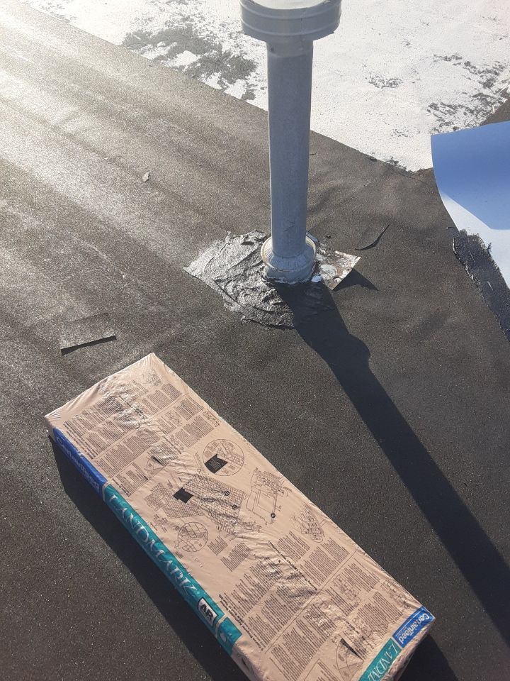 Cardboard box on a flat rooftop near a white vent pipe, with snow along the roof edge.