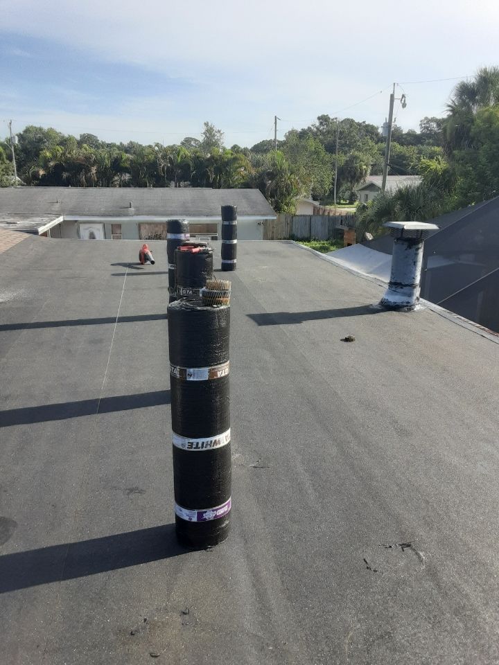 Flat rooftop with black vent pipe in foreground and distant chimneys under a bright sky.