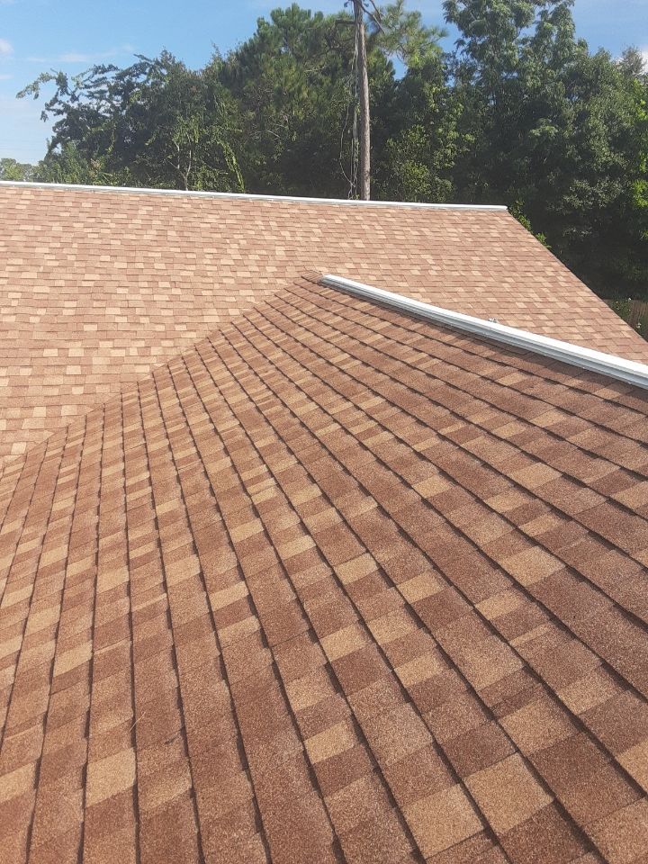 Brown shingled roof under blue sky with trees in the background
