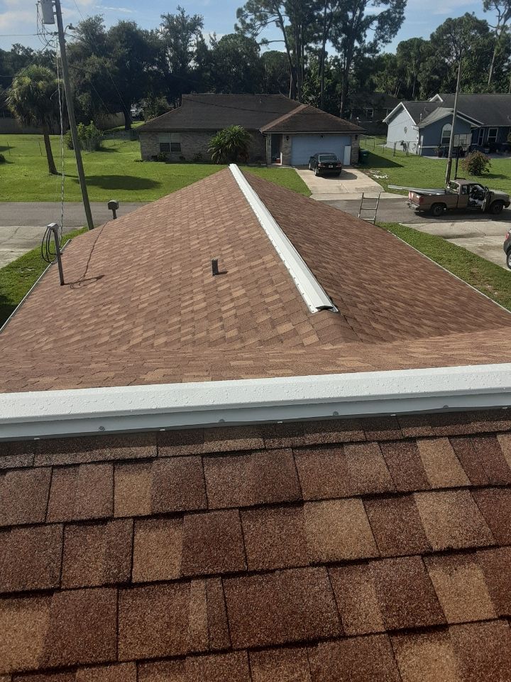 Roof view with reddish shingles and a white ridge vent, overlooking a suburban neighborhood.