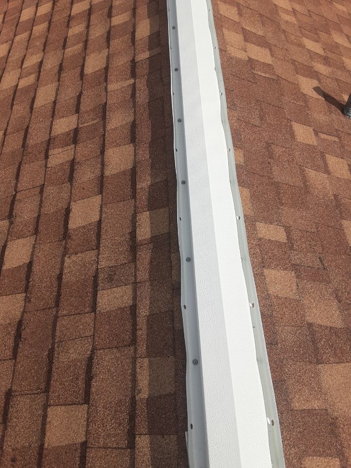 Close-up of a brown shingled roof with a white ridge cap running down the center.