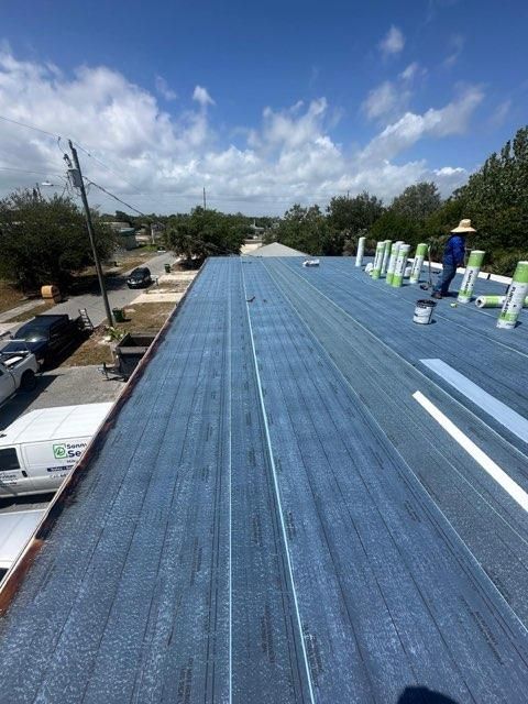 Blue roof under construction with workers on top, viewed from above on a sunny day