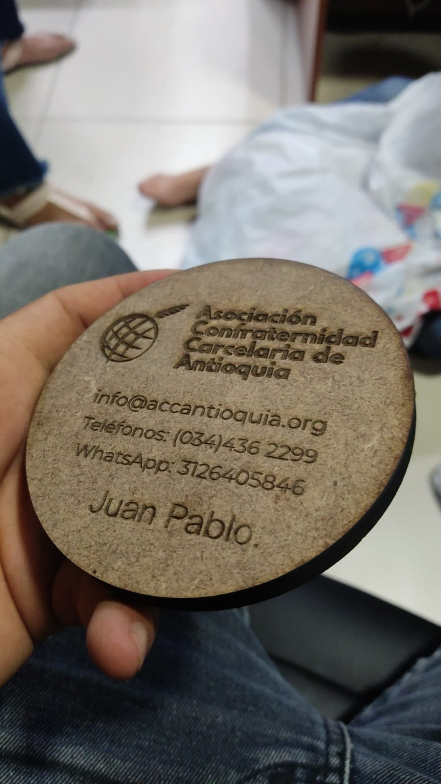 Placa redonda de madera grabada, sostenida en la mano, con texto en español y el logotipo de un globo terráqueo.