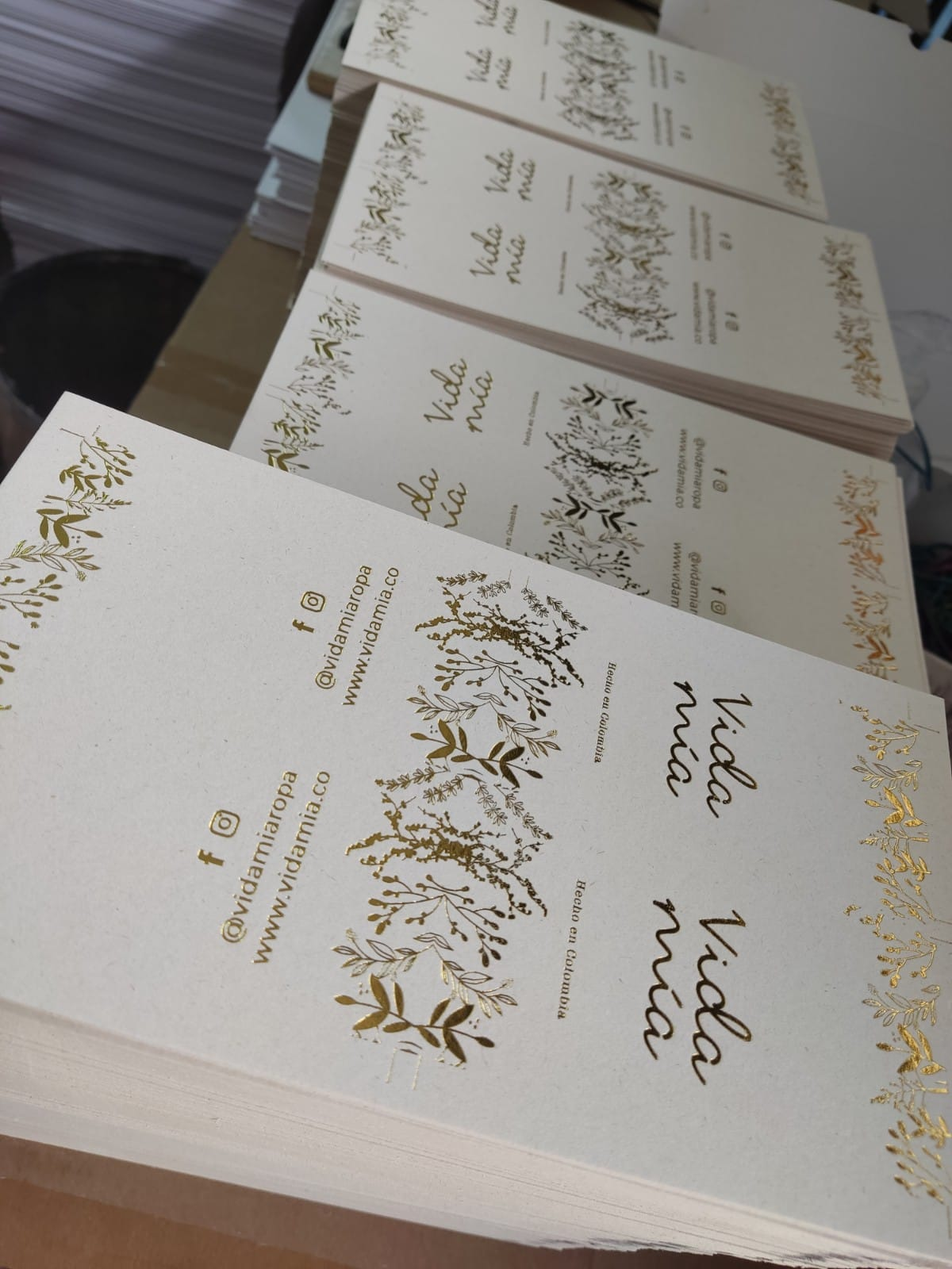 Montones de invitaciones de boda color crema con letras doradas y detalles florales sobre una mesa.