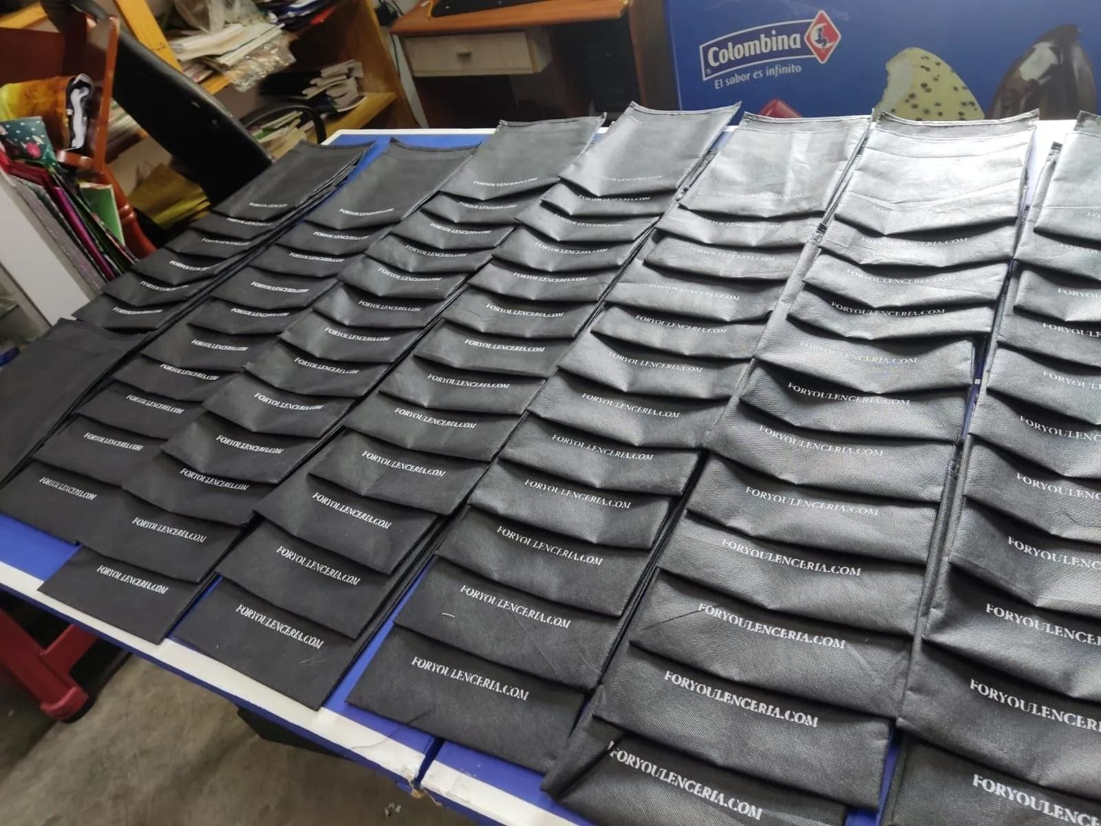 Filas de mangas aislantes negras con logotipos blancos dispuestas sobre una mesa en un taller.
