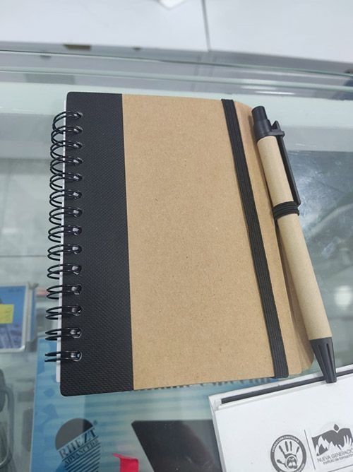 Un cuaderno de espiral con tapas negras y color kraft y un bolígrafo sobre un escritorio de cristal.