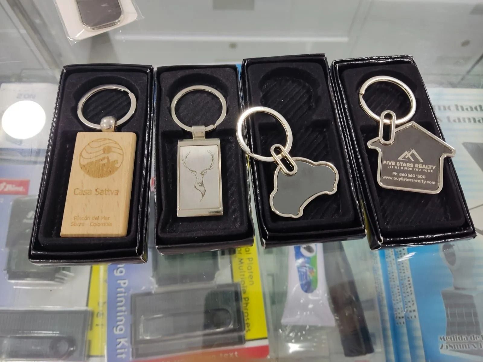 Cuatro llaveros metálicos de recuerdo en bandejas negras de exhibición sobre un mostrador de cristal.