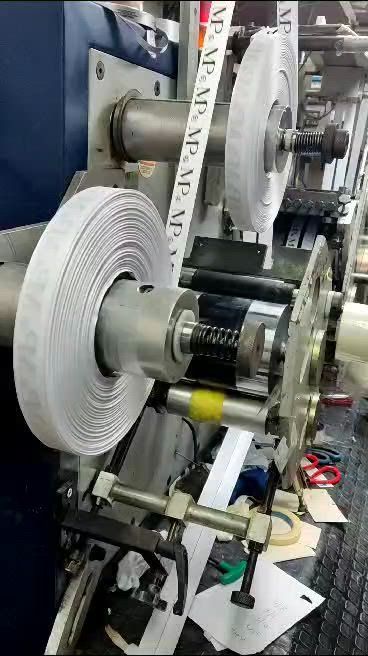 Máquina industrial con grandes rollos de material blanco sobre un eje metálico en un taller.