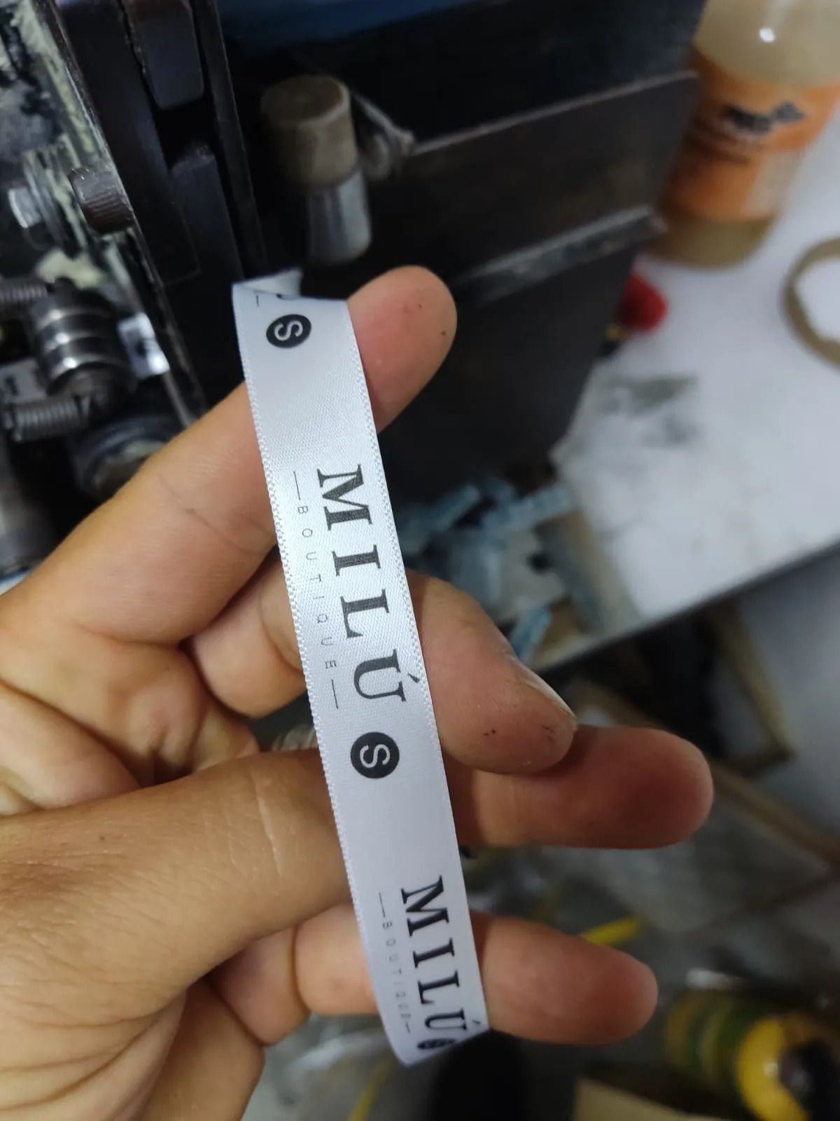 Mano sosteniendo una correa de reloj MILUS blanca con letras negras en un taller.