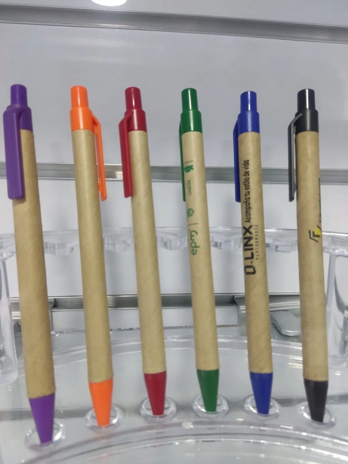 Cinco bolígrafos de colores colocados en fila sobre una superficie gris.
