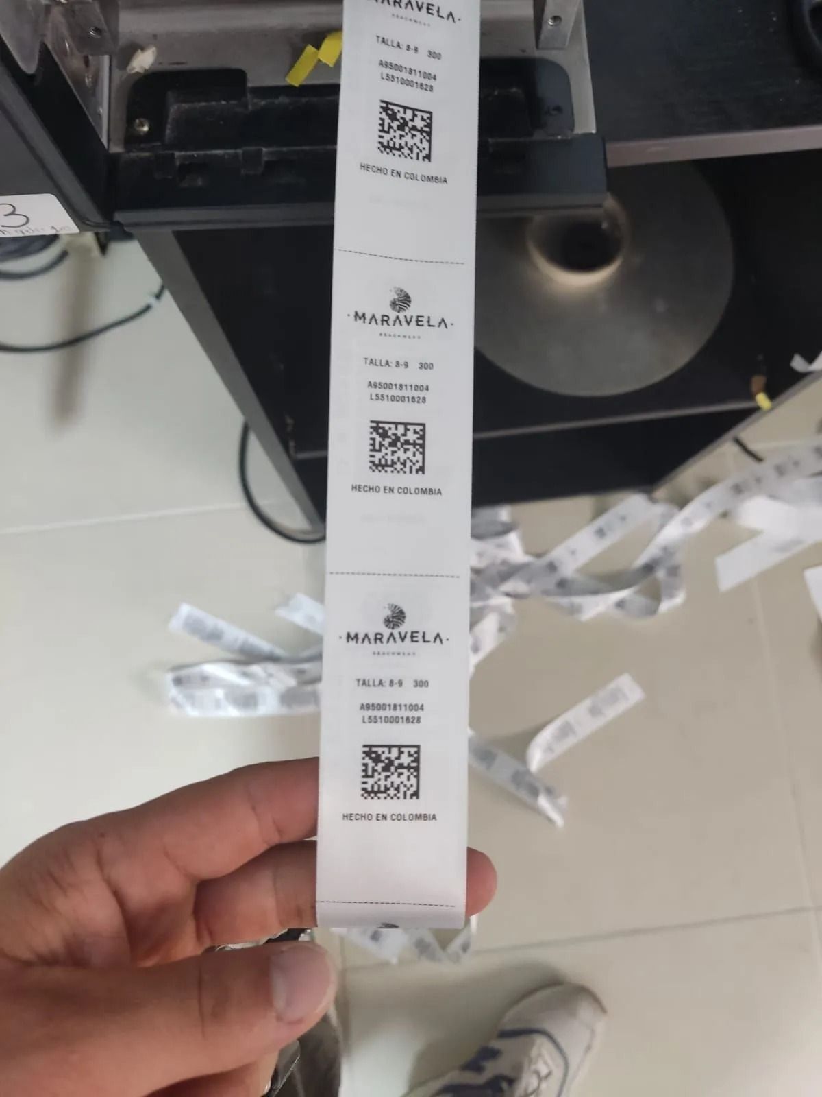 Una mano sostiene una etiqueta de producto con código QR blanco frente a un estante y un expositor de la tienda.