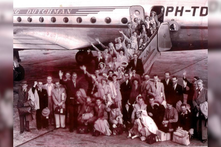 Group of families from Dutch Dredging Co. arriving in Melbourne, with image taken with aircraft in background as they are disembarking.