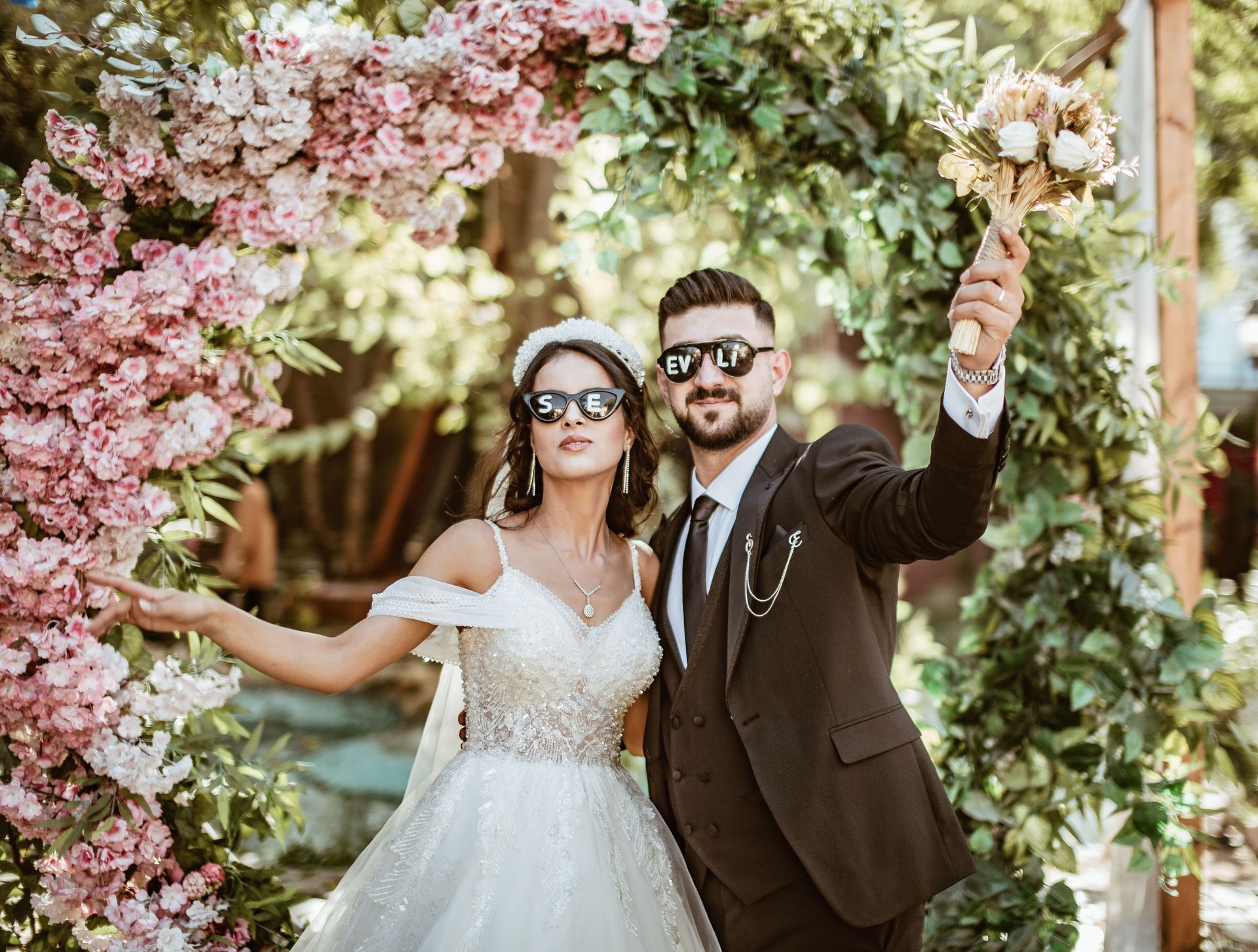 Wedding party posing on a red carpet outdoors, with a bride in white and guests in blue suits and dresses