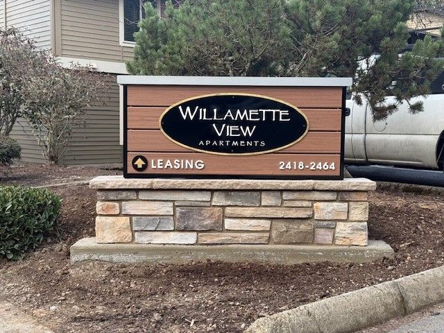 Willamette View Apartments leasing sign on a stone base beside a curb and shrubs