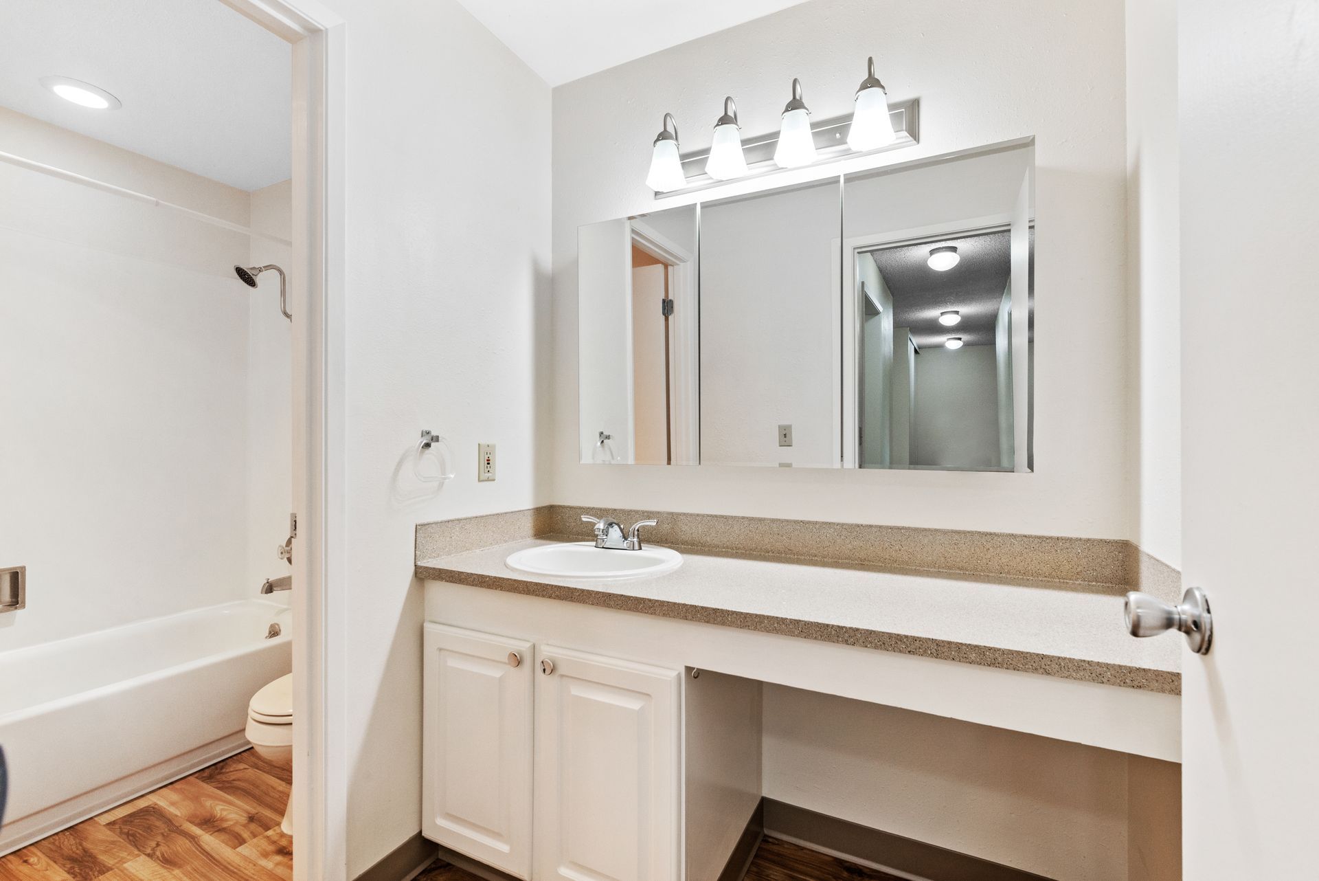 Bathroom vanity with large mirror, granite countertop, and adjacent bathtub in a bright white interior