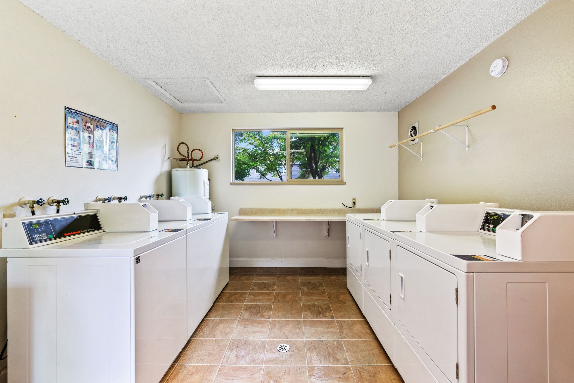 Bright laundry room with white washers and dryers along both walls and a window at the back