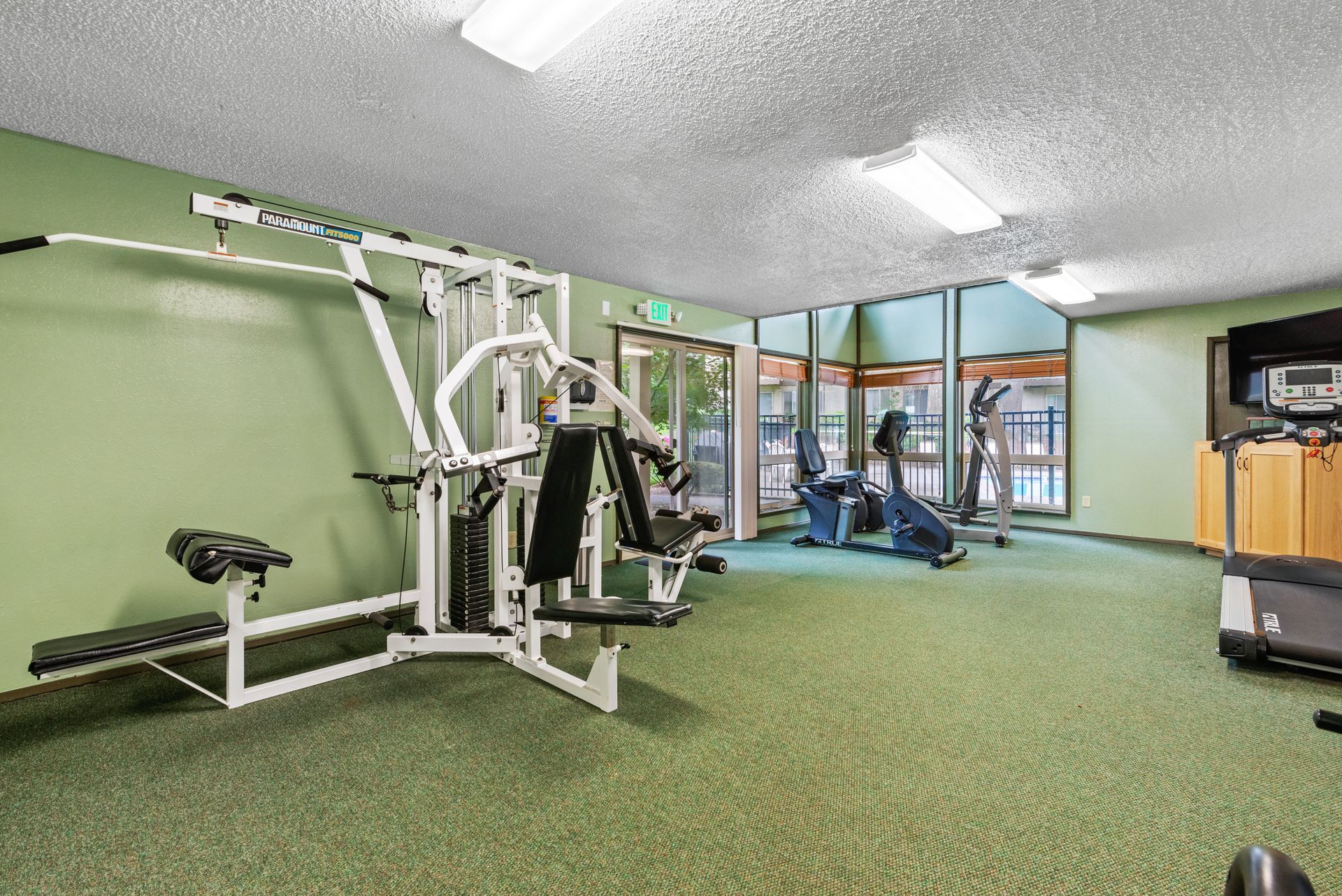 Indoor gym with white exercise machine, green carpet, and large windows.