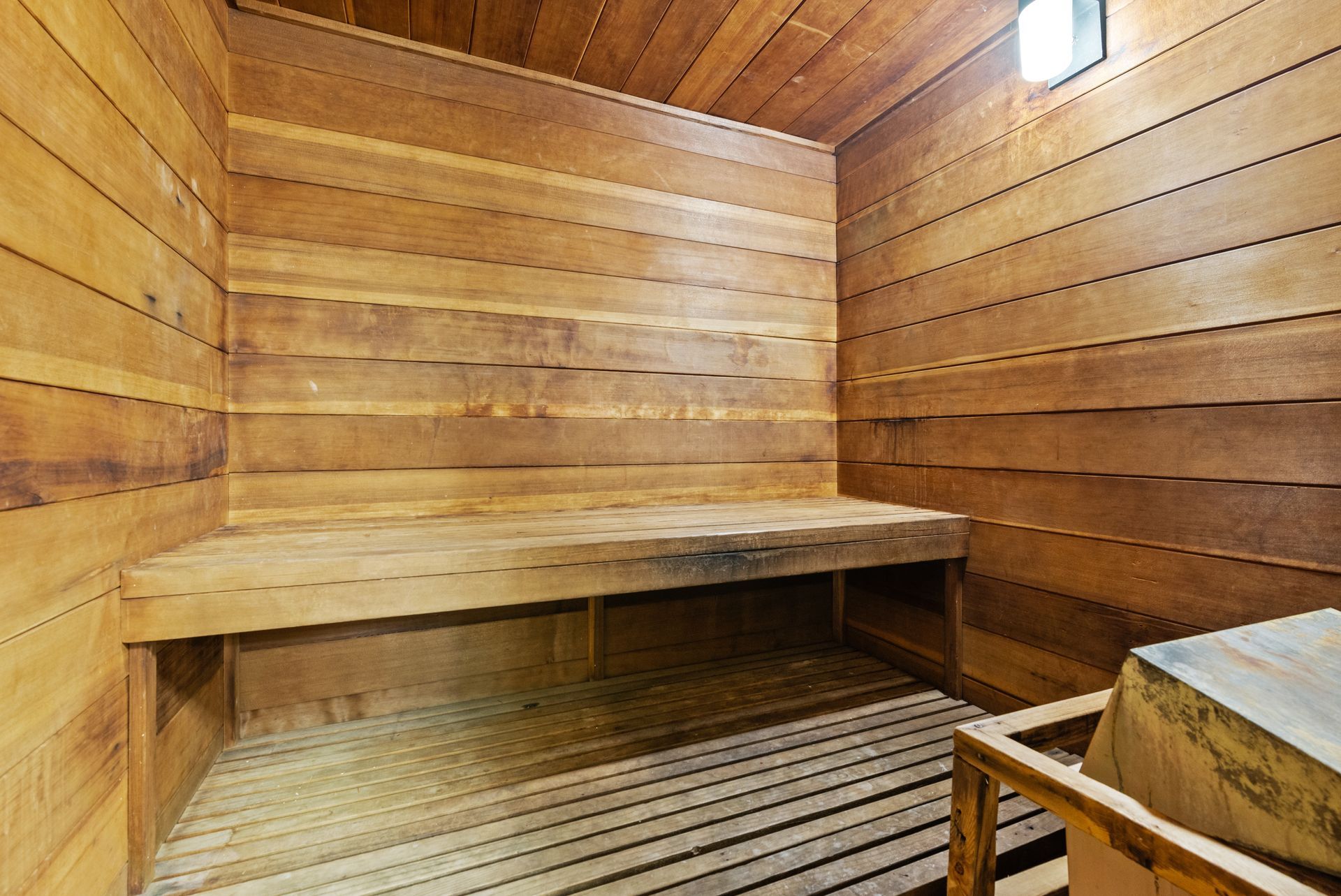 Wood-paneled sauna with wooden benches and slatted floor, warmly lit by a small window.