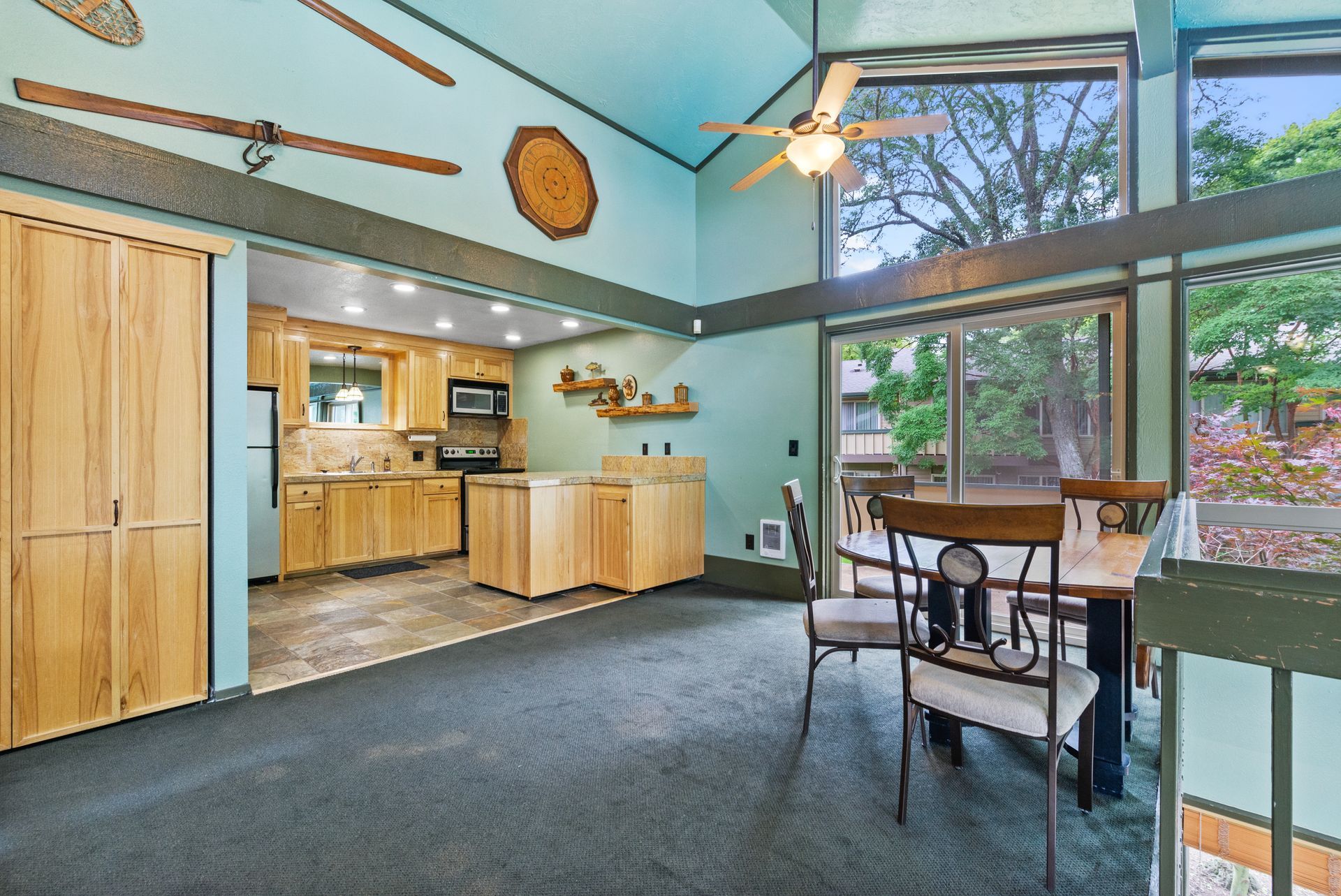 Bright living room with vaulted ceiling, large windows, wood cabinets, and a small dining table.