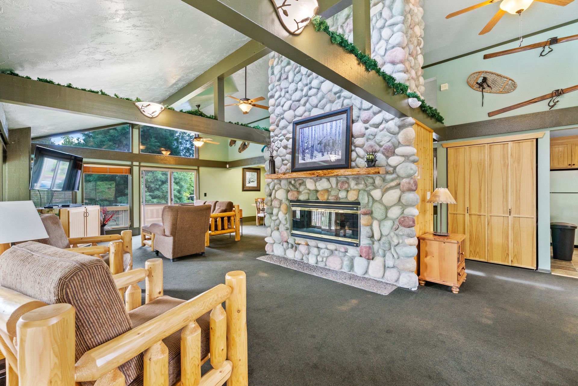 Rustic lodge-style living room with stone fireplace, wood beams, and wicker chairs